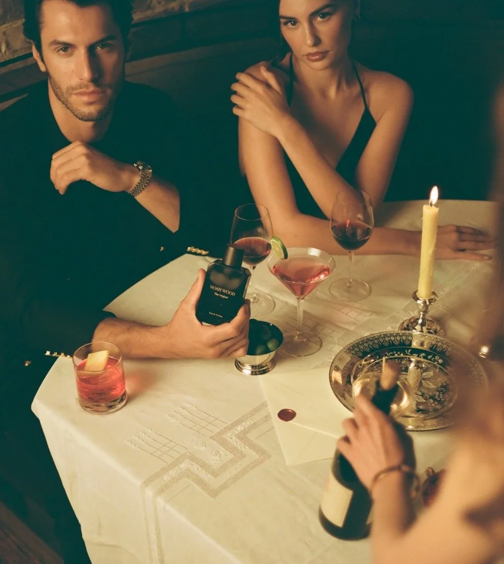 Two friends at a candlelit dinner table, one holding a bottle of The Original, with a negroni and wine glasses on the table